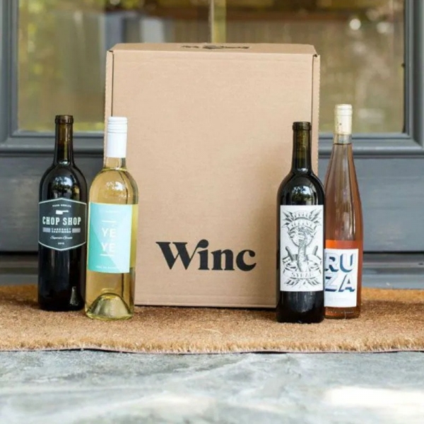 Winc Wine Subscription box and three wine bottles on a carpet in front of door