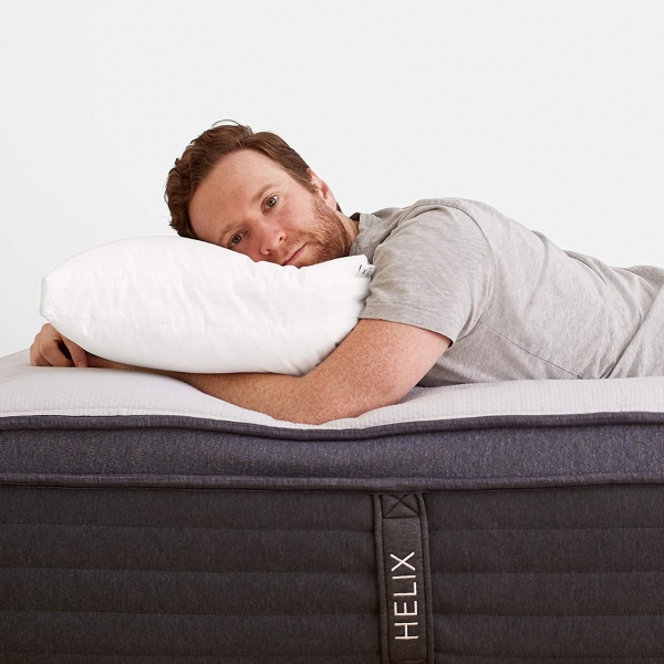 A man lying on a Helix mattress with his head on a white Helix Adjustable Pillow with his arms lying underneath
