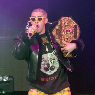bad bunny performing on stage at american airlines arena in yellow plaid pants a graphic black tee and leather jacket