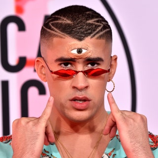 bad bunny with a prosthetic third eye red lipshaped glasses and his pinky pointed towards his face